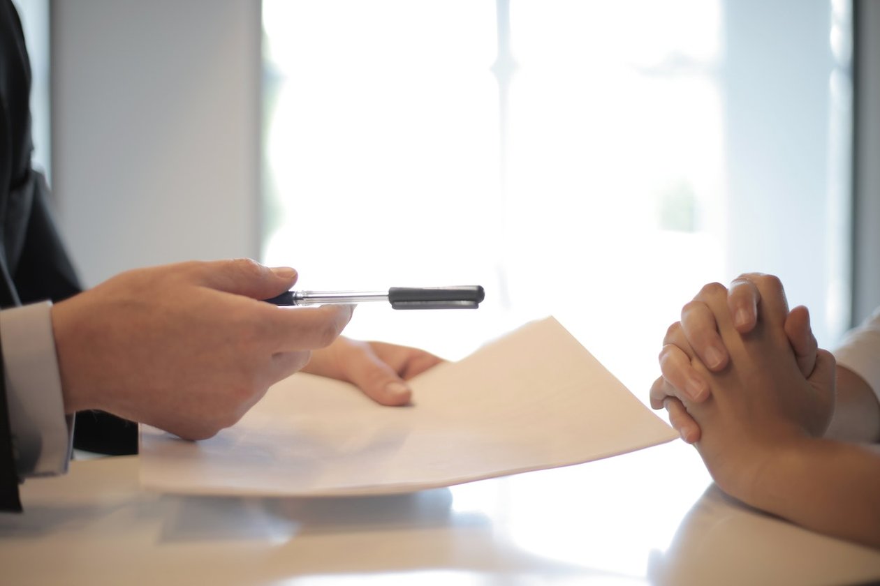 Person handing a pen and paper over to another person to sign.